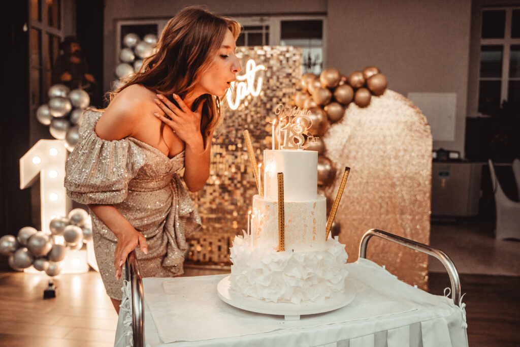 Kobieta dmuchająca świeczki na eleganckim torcie urodzinowym podczas przyjęcia.