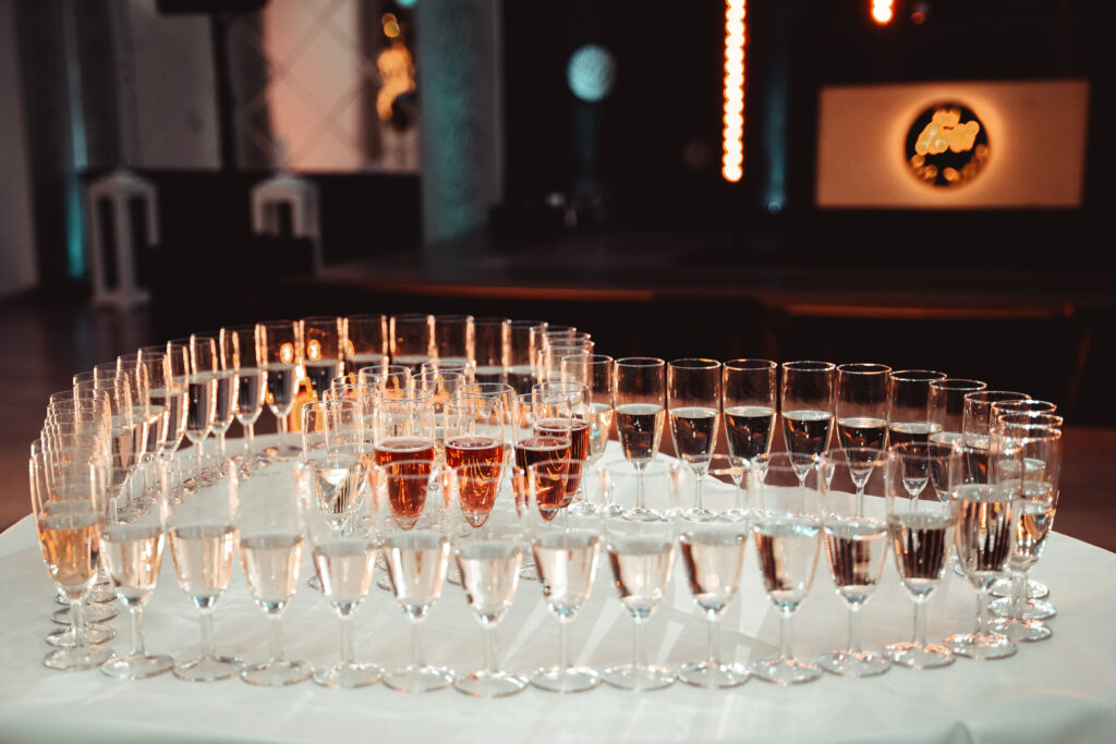 Elegancko ustawione kieliszki na stole na weselu, gotowe do toastu, z różnymi napojami w tle.