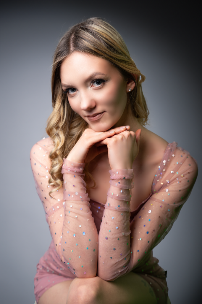 Młoda dziewczyna o blond włosach, opierająca głowę o dłonie w studio fotograficznym