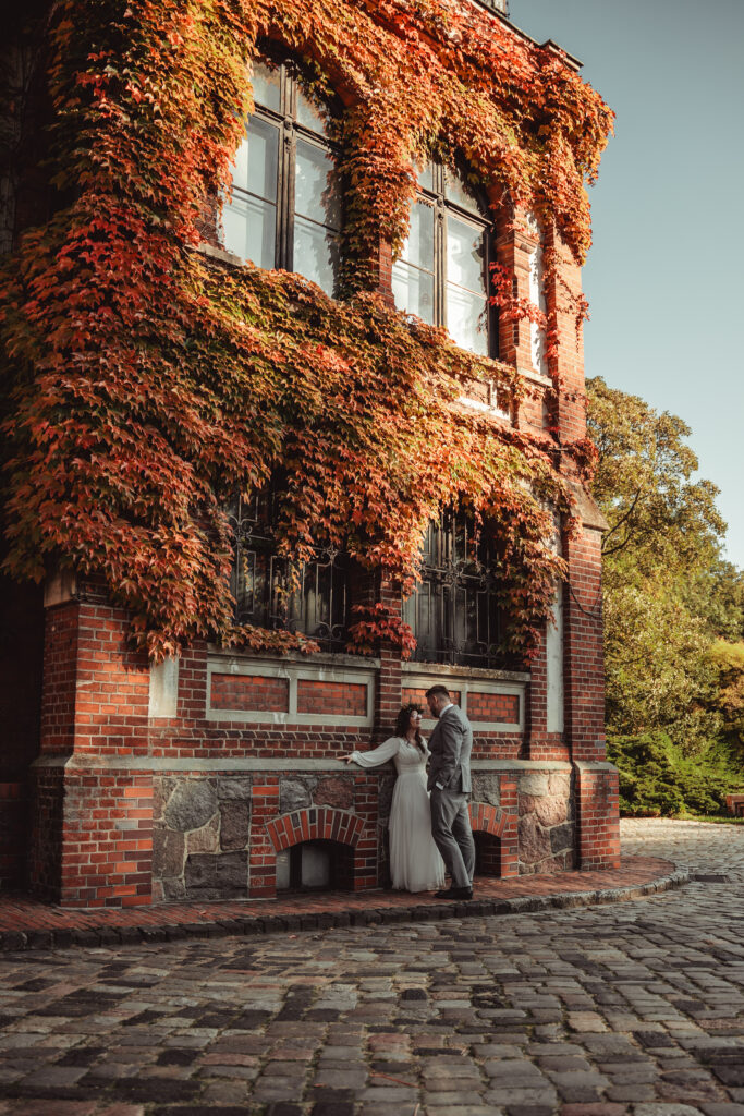 Para młoda na tle zabytkowego budynku obrośniętego przez jesienne liście