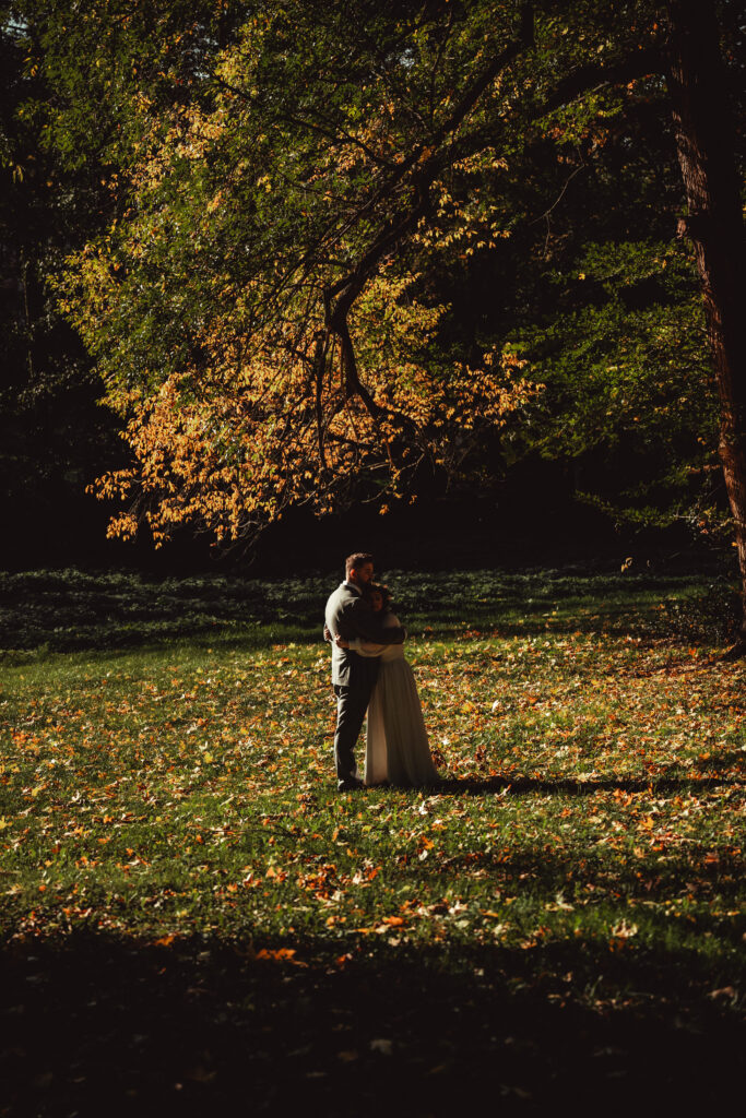 Para młoda obejmuje się w parku w jesiennej scenerii, wśród kolorowych liści.